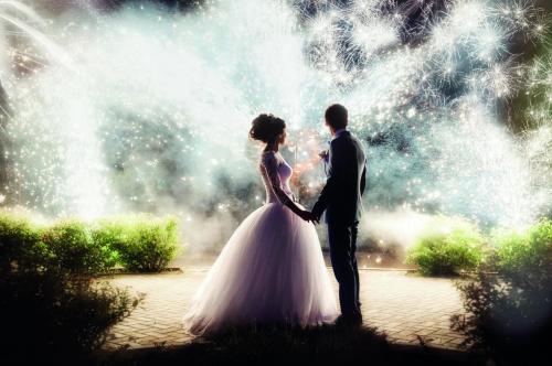 Newlyweds stand against the background of the fireworks at night